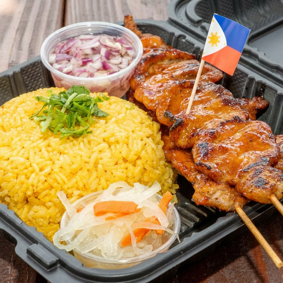 Filipino meal with yellow rice, grilled glazed skewers, pickled vegetables, onions, and a Philippine flag in a takeout tray.